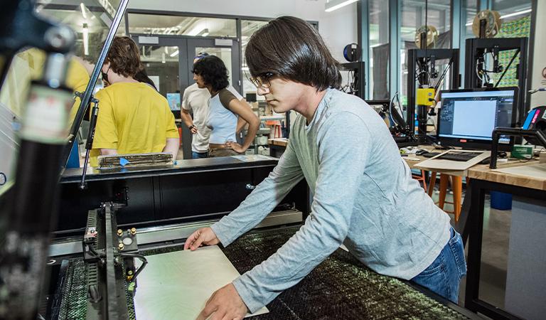 A Makerspace Steward prepares a large piece of paper on a machine.